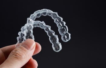 Hand holding two transparent retainers on black background. Invisalign orthodontics concept